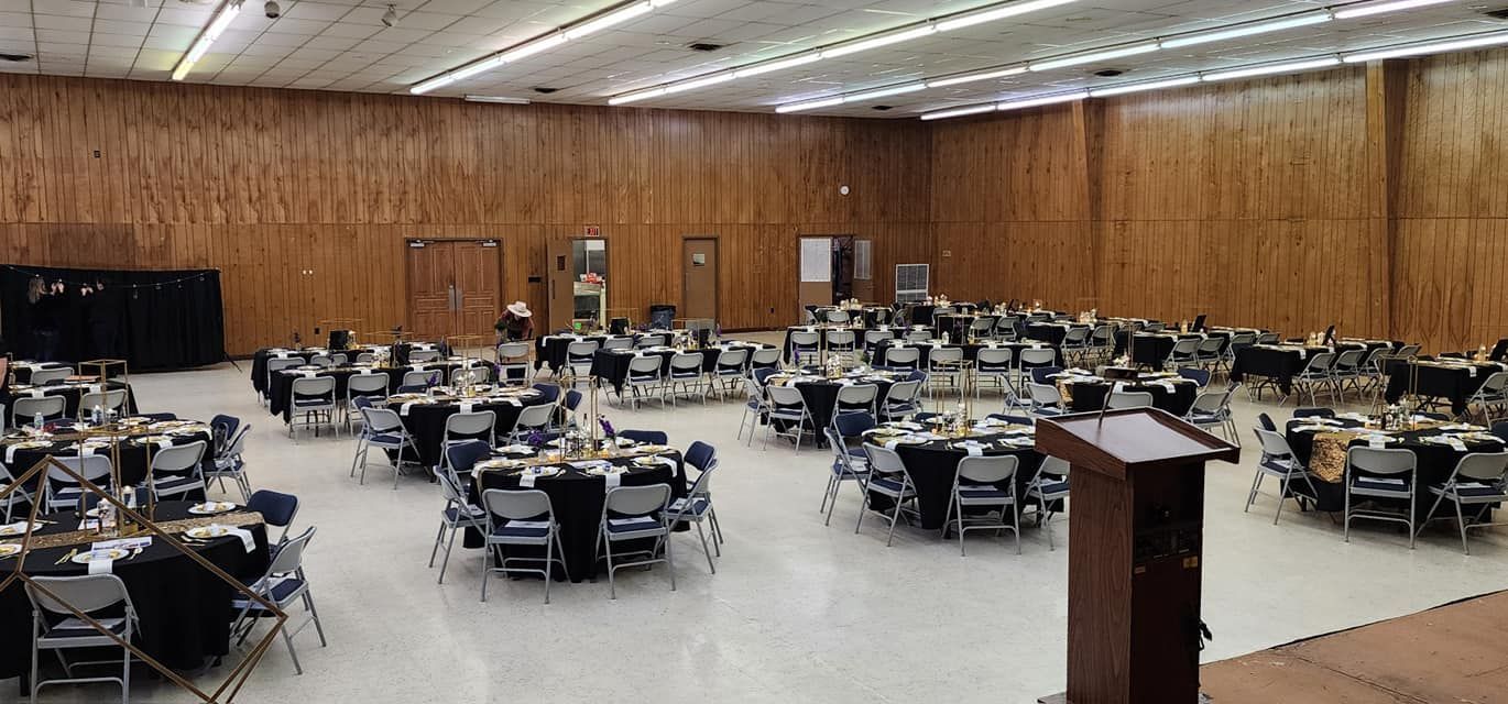 Large room set with round tables and chairs for an event. Podium in foreground. Wood paneling on walls.