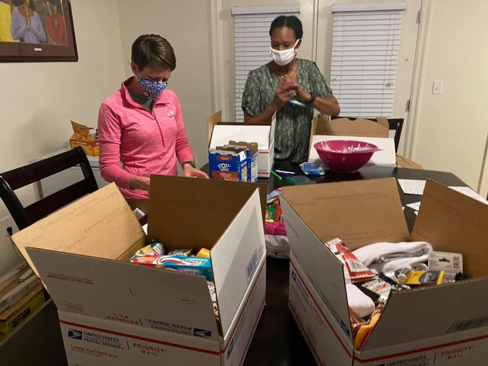 Two people in masks packing boxes with food and supplies at a table.