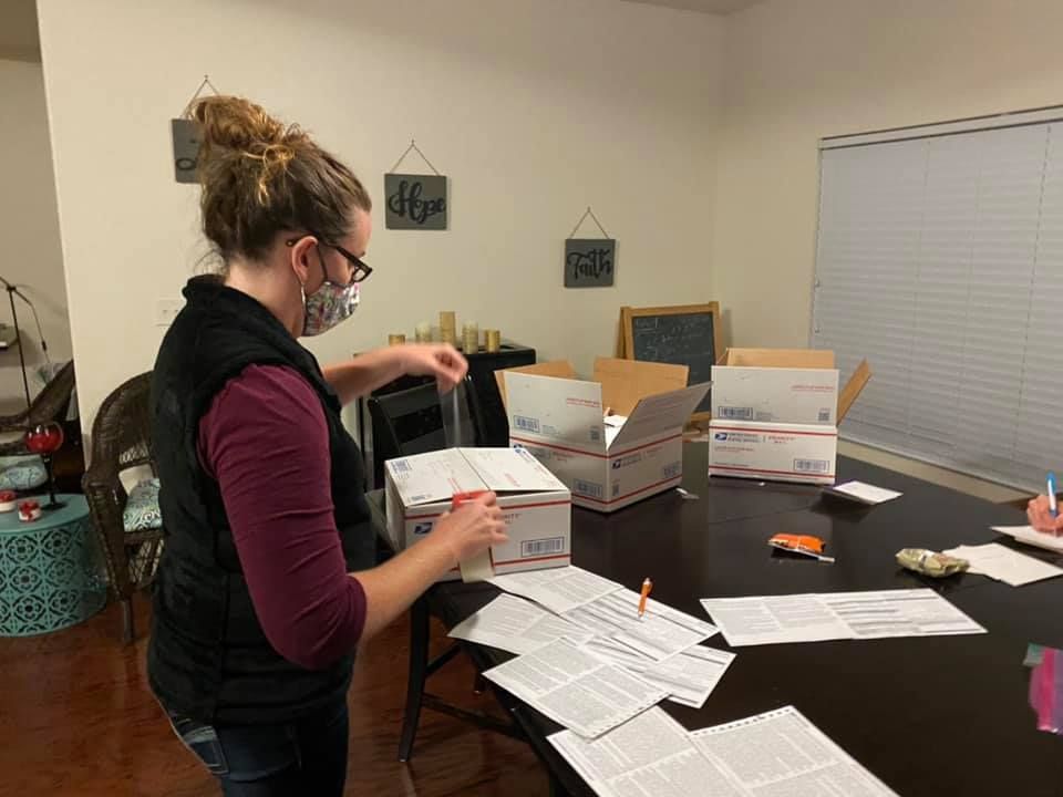 Woman wearing a face mask packs a box with shipping labels on a table.