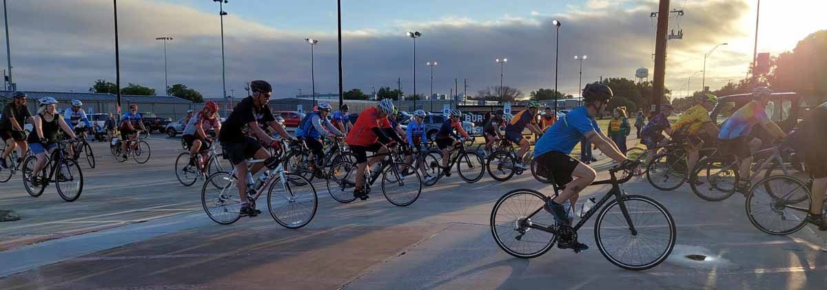 Cyclists in a race on a paved road at dusk, with the sky overcast.