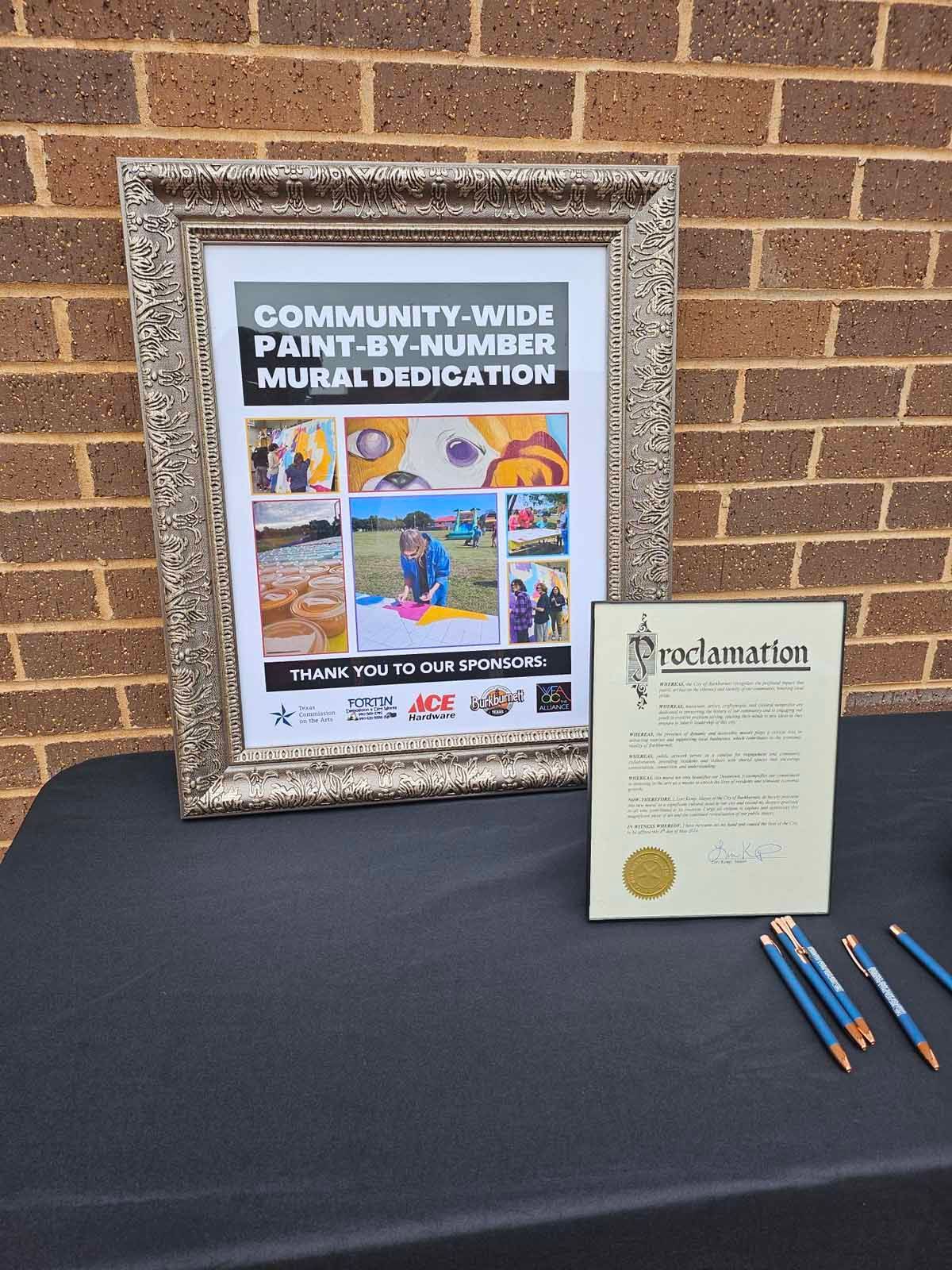 A framed poster and a proclamation are on a table. Pencils are nearby.