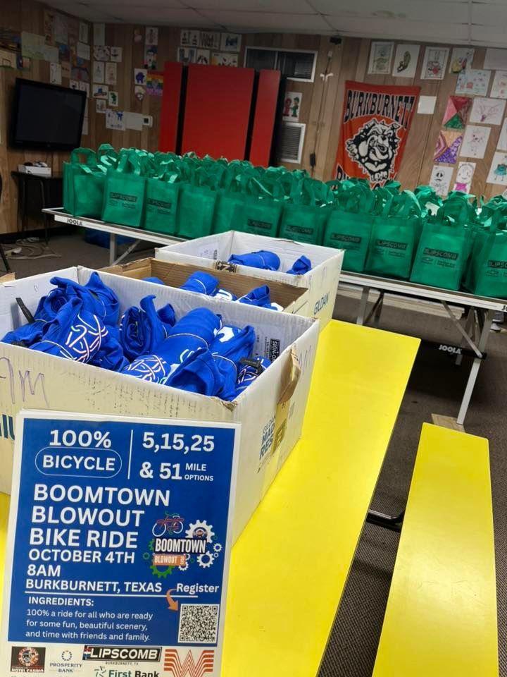 Boxes of blue shirts, green bags, and yellow tables for a bike ride event.