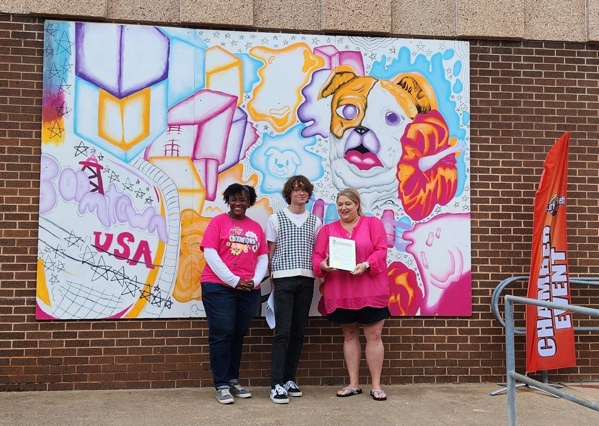 Three people stand in front of a colorful mural of a dog and abstract shapes.