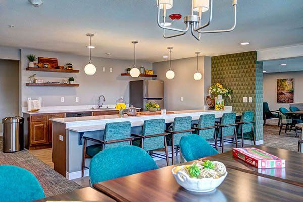 A dining room with tables and chairs and a kitchen in the background.