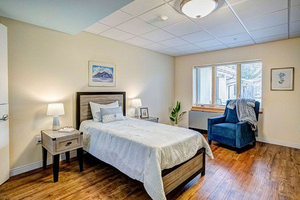 A bedroom with a bed , chair , nightstand and lamps.