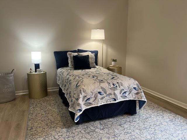 A bedroom with a bed , nightstand , lamp and rug.