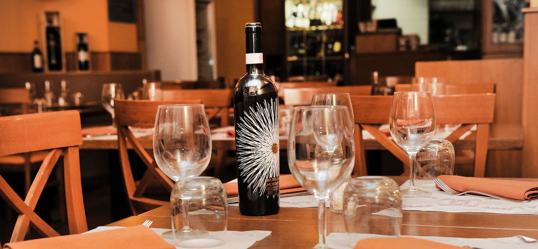 Tavolo del ristorante apparecchiato con bicchieri da vino e una bottiglia di vino.