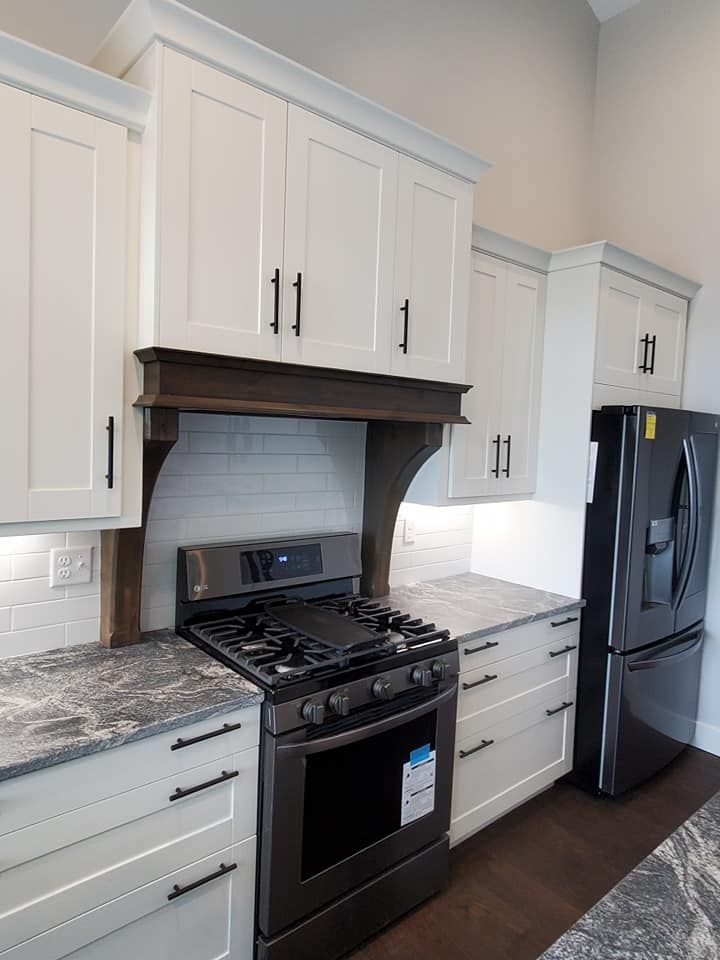 Modern kitchen with white shaker cabinets, dark wood vent hood, stainless steel stove, and granite countertops.
