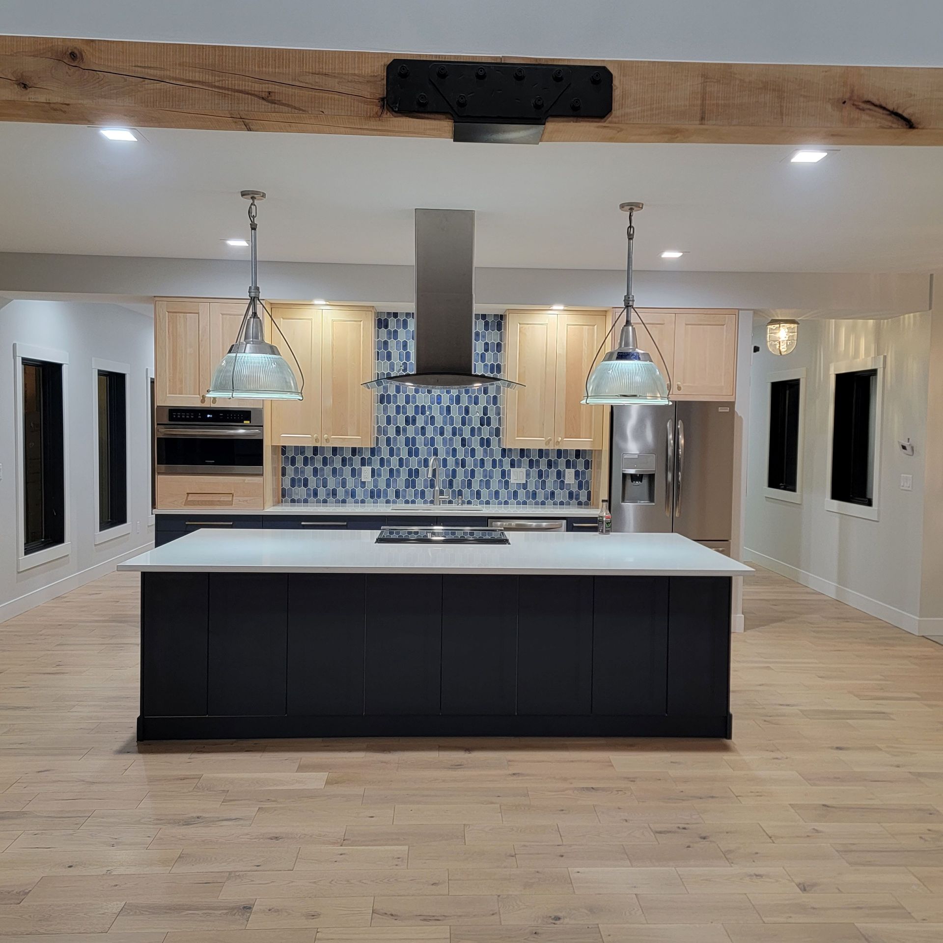 A kitchen with a dark-blue island, light wood cabinets, stainless steel appliances, and a blue mosaic tile backsplash.