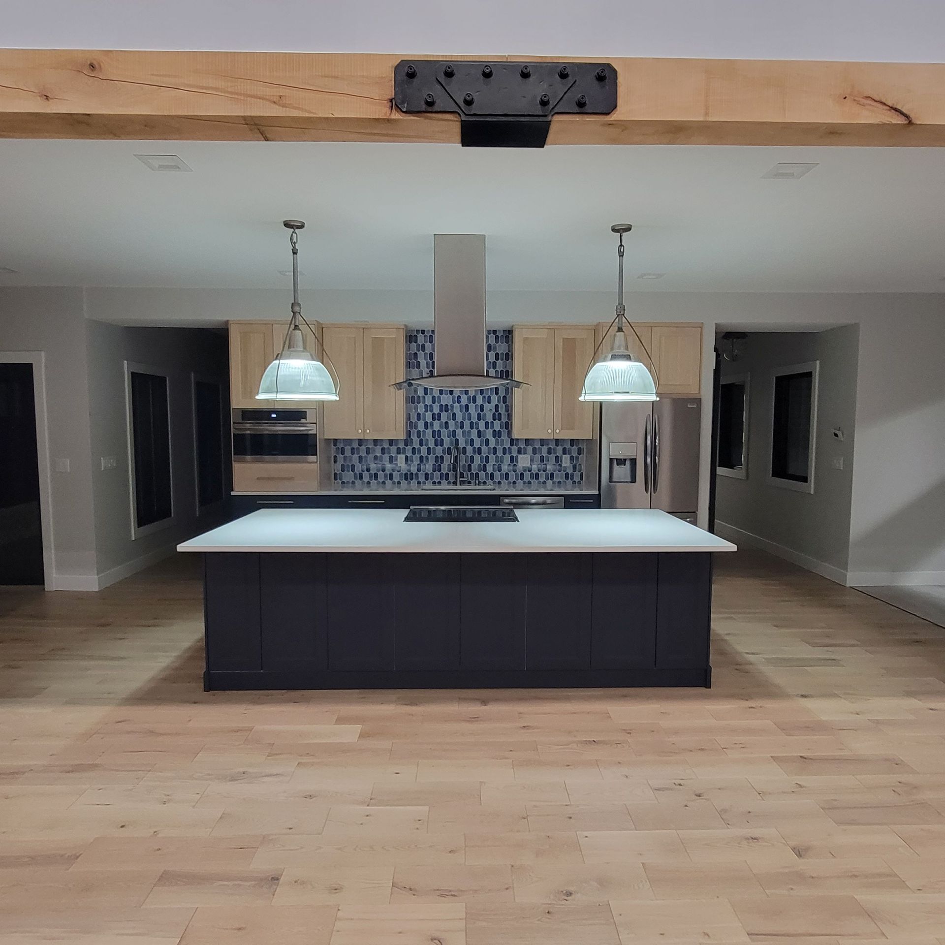 Modern kitchen with a dark blue island, light wood cabinetry, blue patterned backsplash, and two hanging pendant lights.