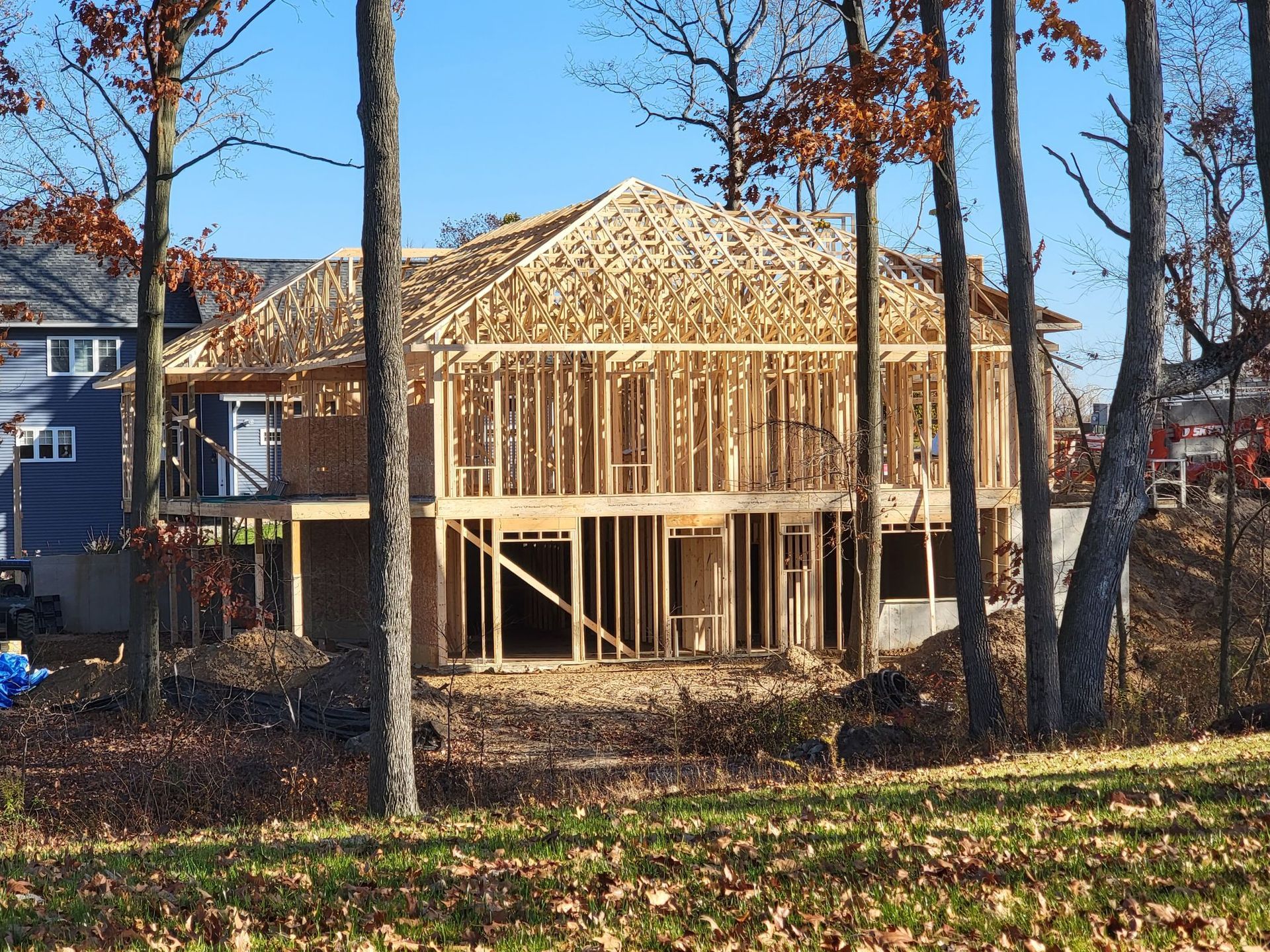 The wooden frame of a two-story house under construction, surrounded by trees on a sunny day.