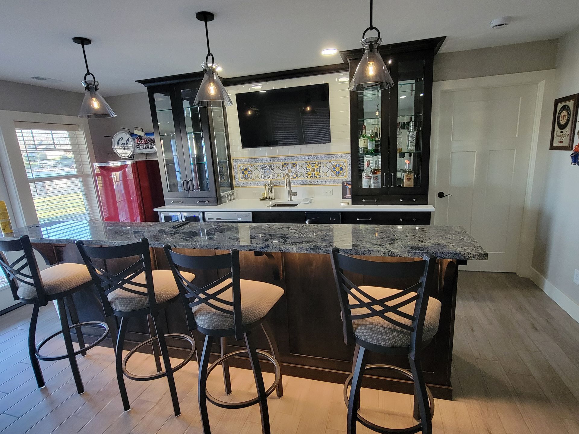 A home bar featuring dark wood cabinets, granite countertops, four bar stools, and pendant lighting.