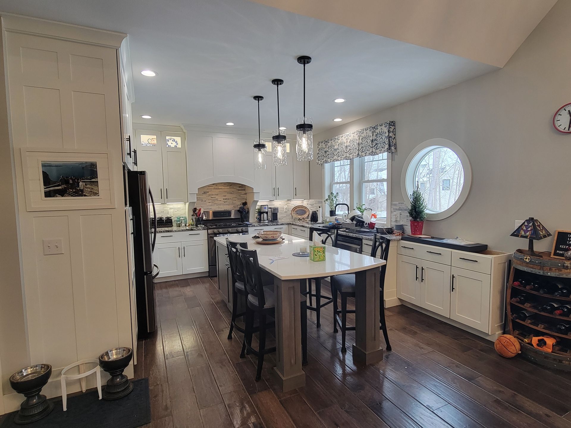 A bright, open kitchen with a center island, white cabinetry, hardwood floors, and three pendant lights.