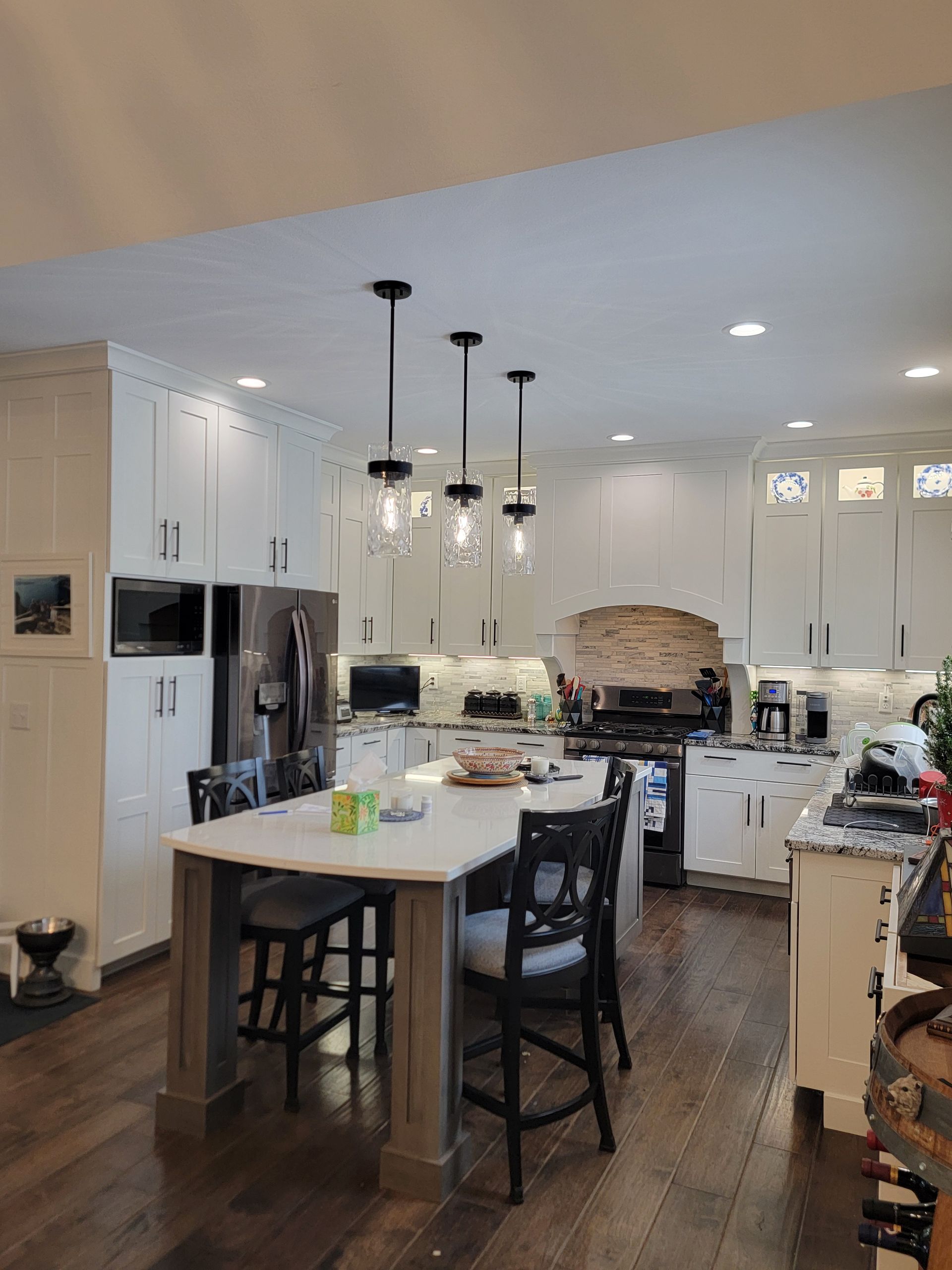 A bright, modern kitchen featuring white cabinetry, a marble-topped island with three pendant lights, and dark wood floors.