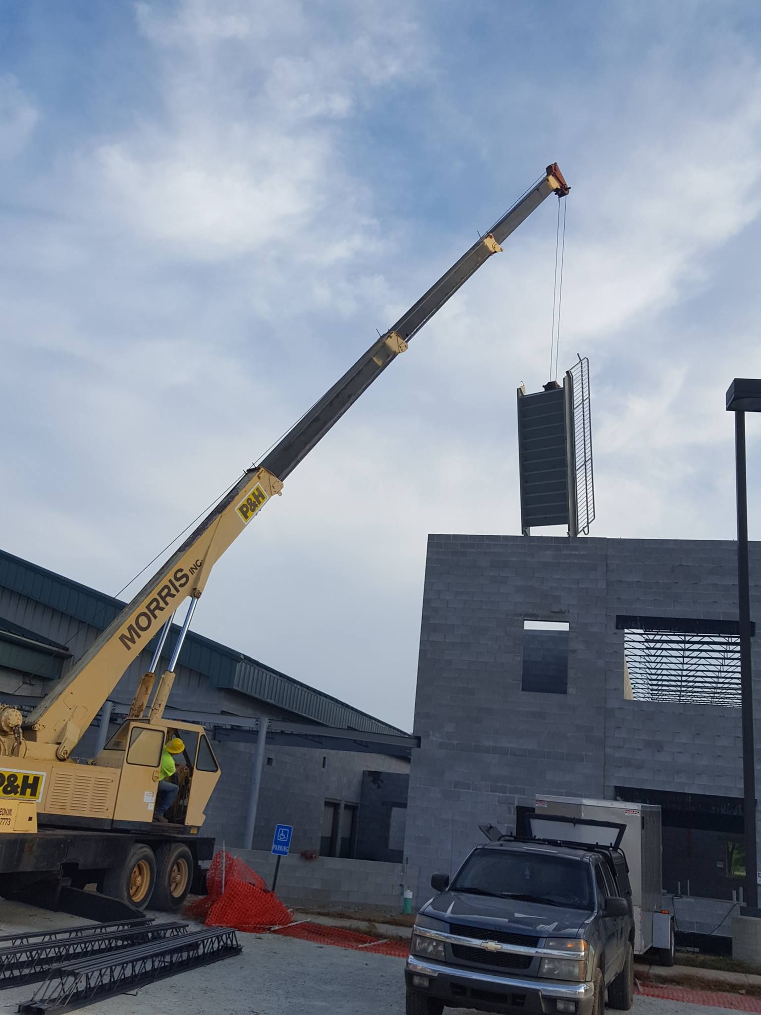 A yellow crane lifts a large sign onto the roof of a gray cinder block building under a cloudy sky.