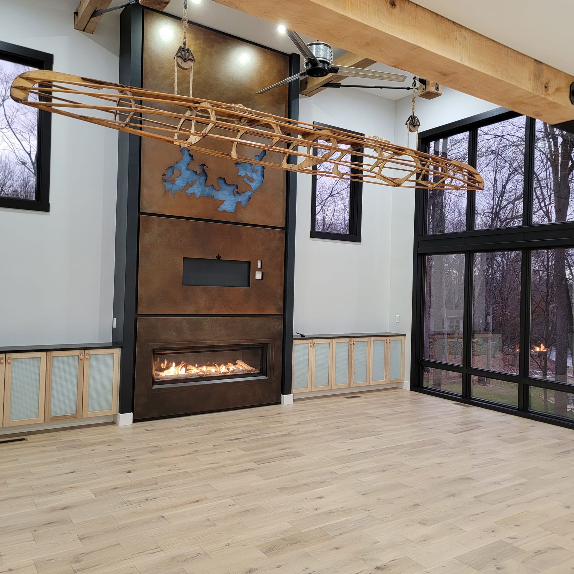 A living room with a linear fireplace, custom metal wall, and a wooden kayak-shaped light fixture hanging from the ceiling.