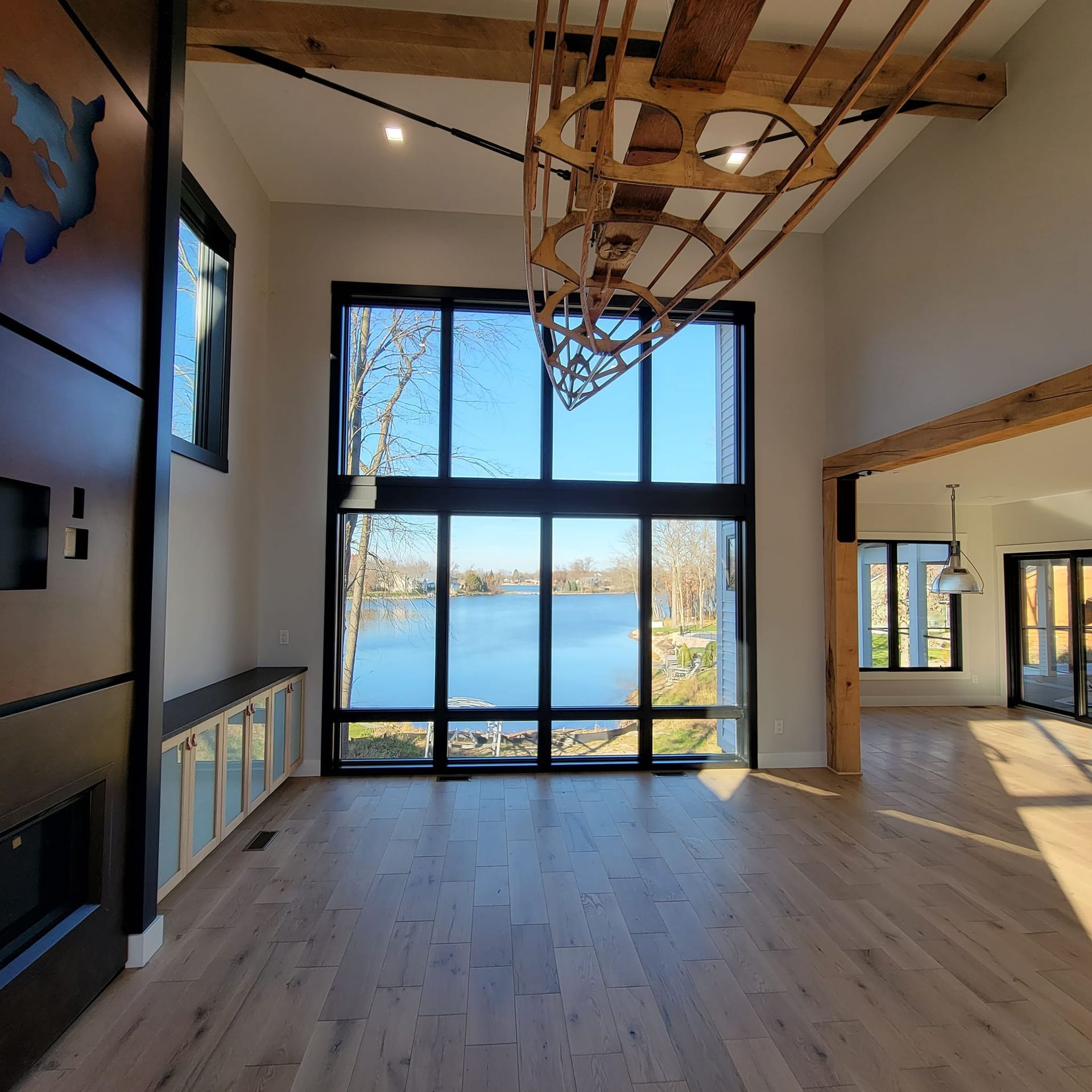 A bright, modern living room featuring a large wall of windows overlooking a lake and a decorative wooden boat structure.