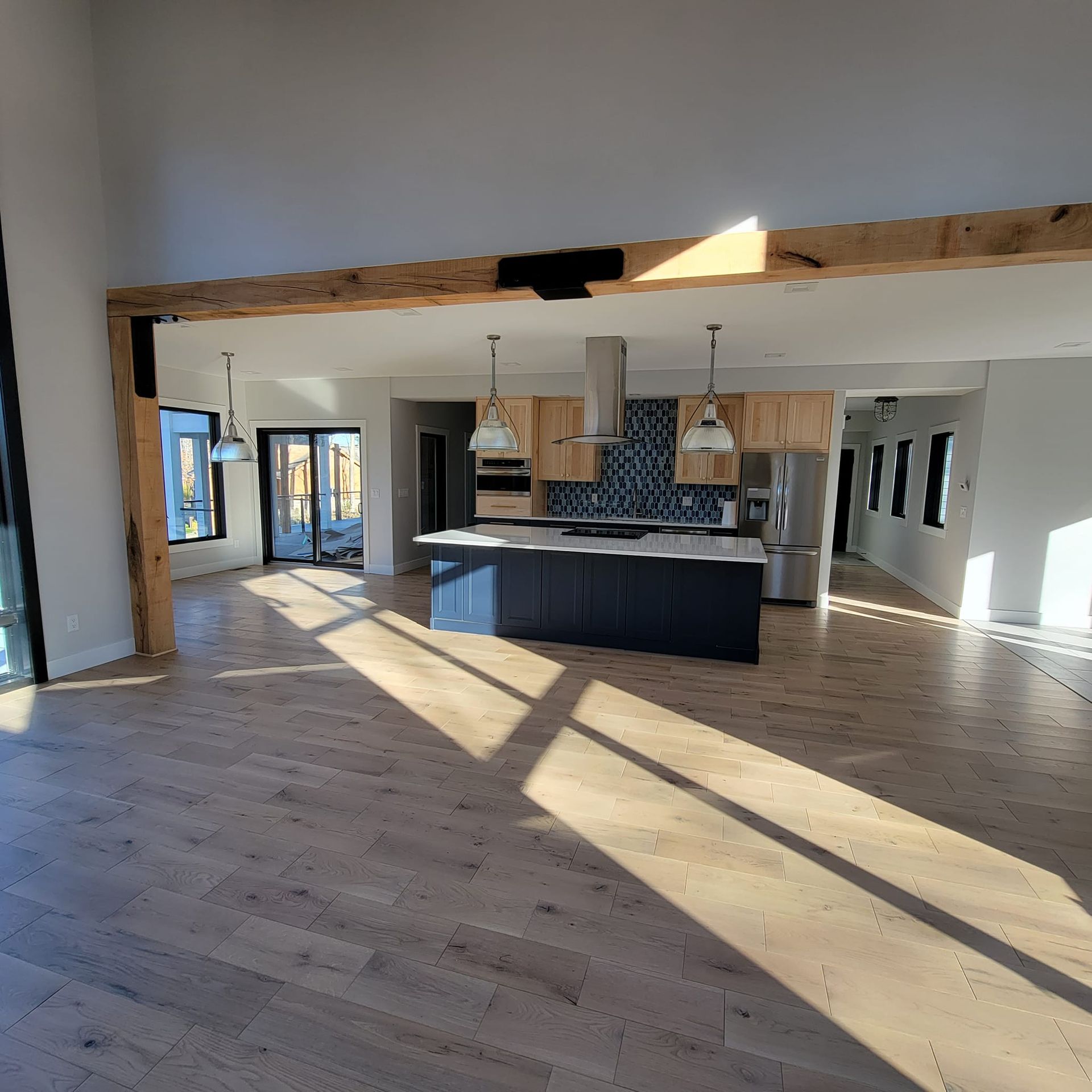 Open floor plan home with light wood floors, a large blue kitchen island, and a prominent rustic wooden support beam.