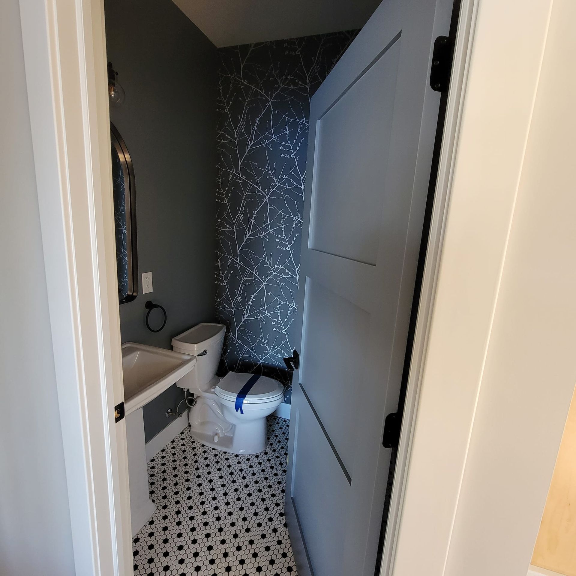 Small half-bath with patterned black-and-white floor tiles, dark gray walls, white fixtures, and a light-gray door.