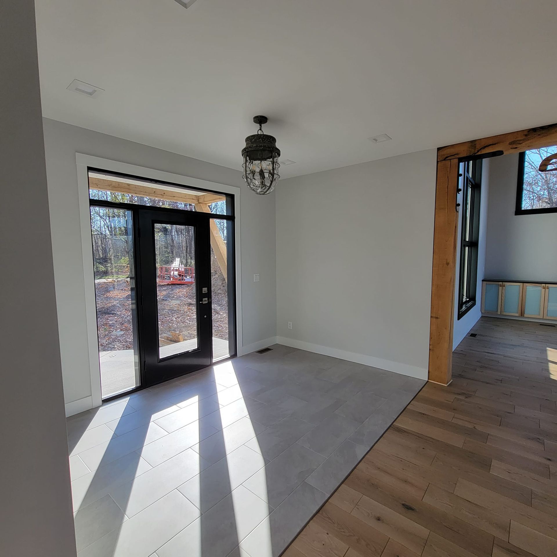 An entryway with gray tiled flooring, a black front door, a hanging lantern light, and an adjacent room with wood floors.