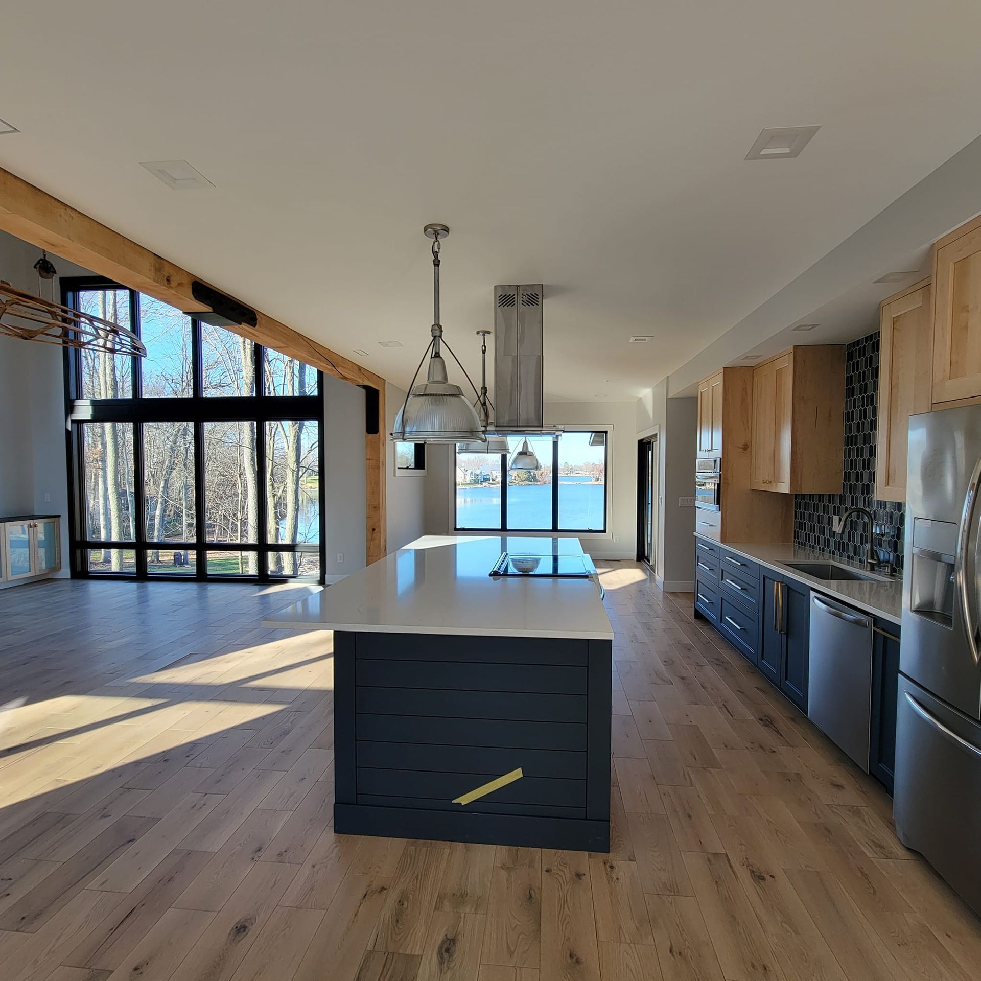 Modern kitchen with a dark blue island, white countertops, wooden cabinets, and large windows overlooking a lake.