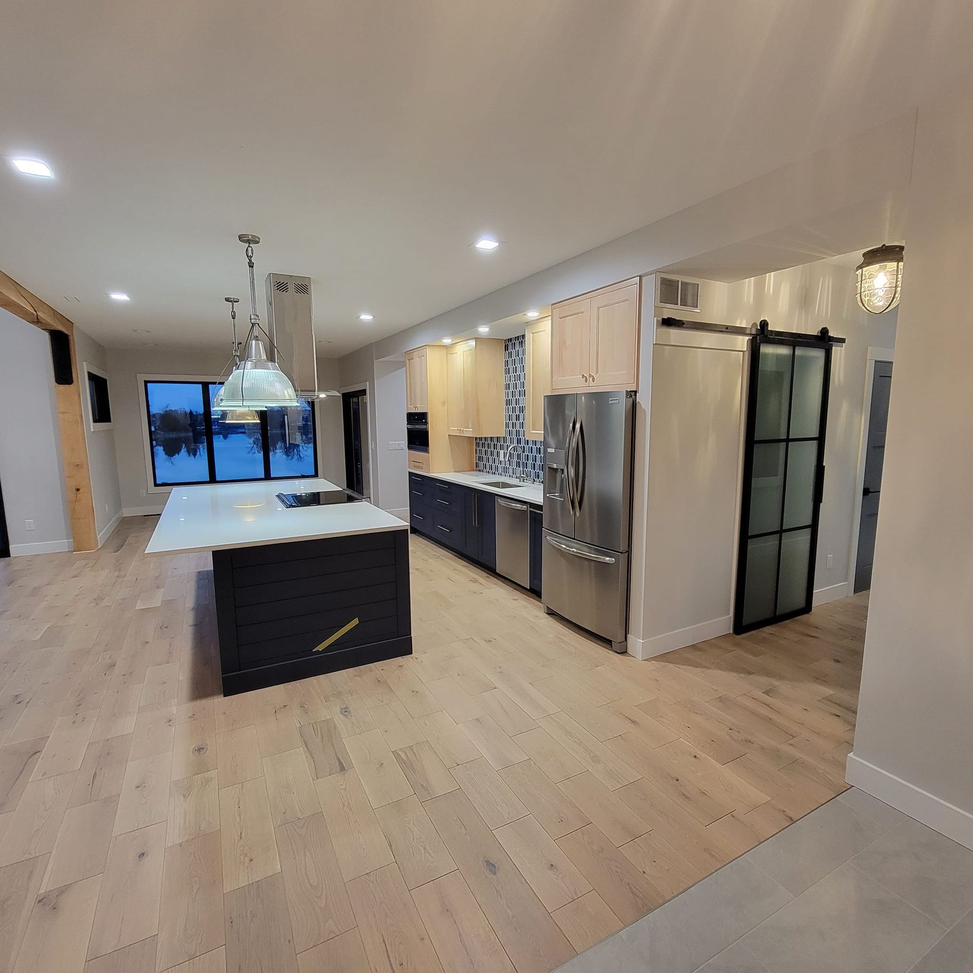 A spacious kitchen featuring a large dark blue island, light wood cabinetry, stainless steel appliances, and a barn door.