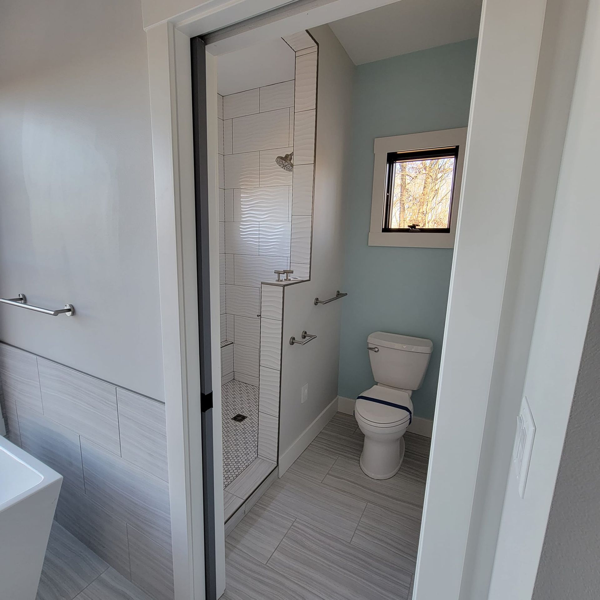 A bright, modern bathroom featuring a walk-in shower with white tile and a separate toilet area with light blue walls.