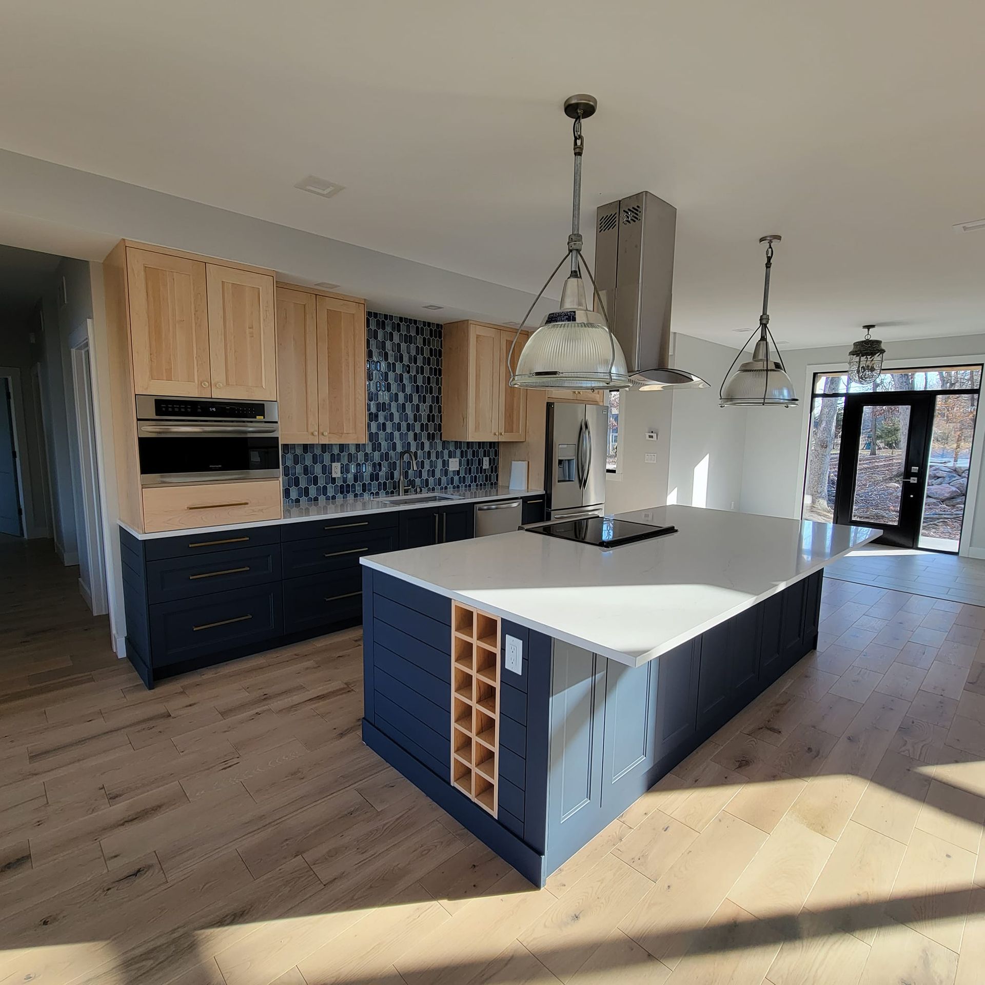 Modern kitchen with natural wood and navy cabinets, white island countertop, tile backsplash, and hanging pendant lights.