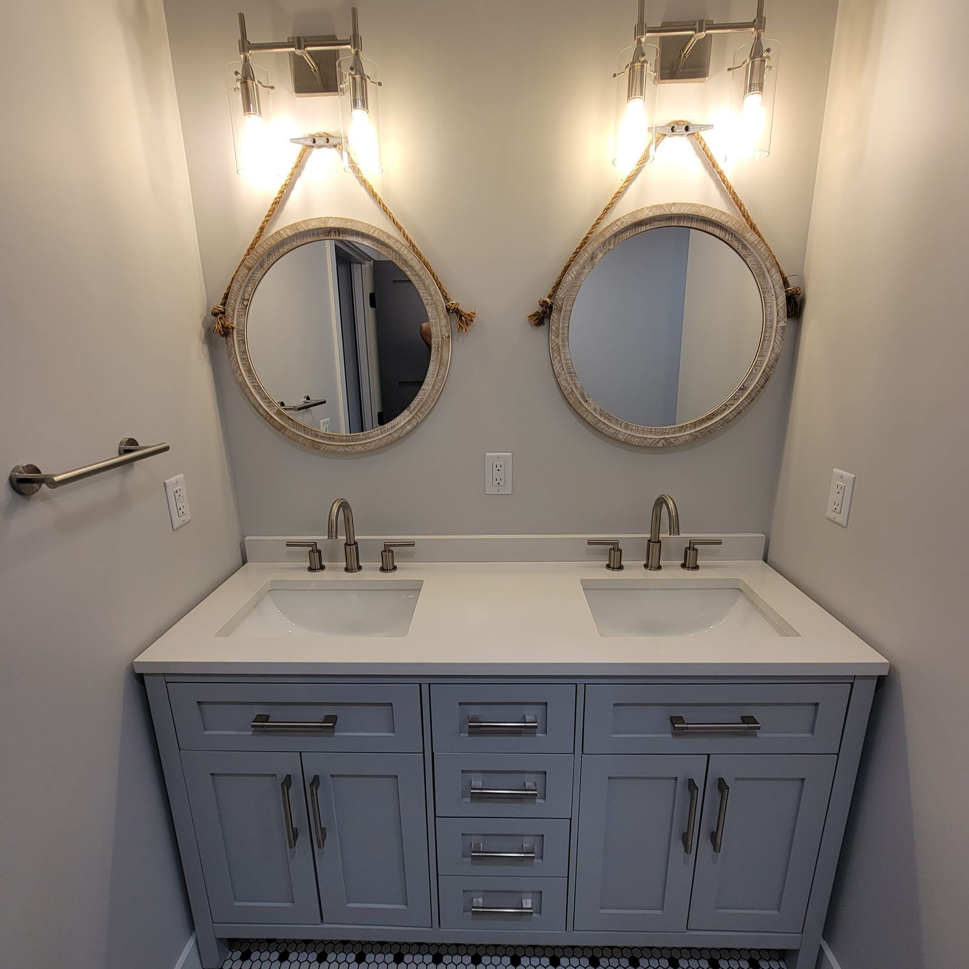 A double-sink bathroom vanity with light gray cabinets, white countertops, rope-framed round mirrors, and wall sconces.