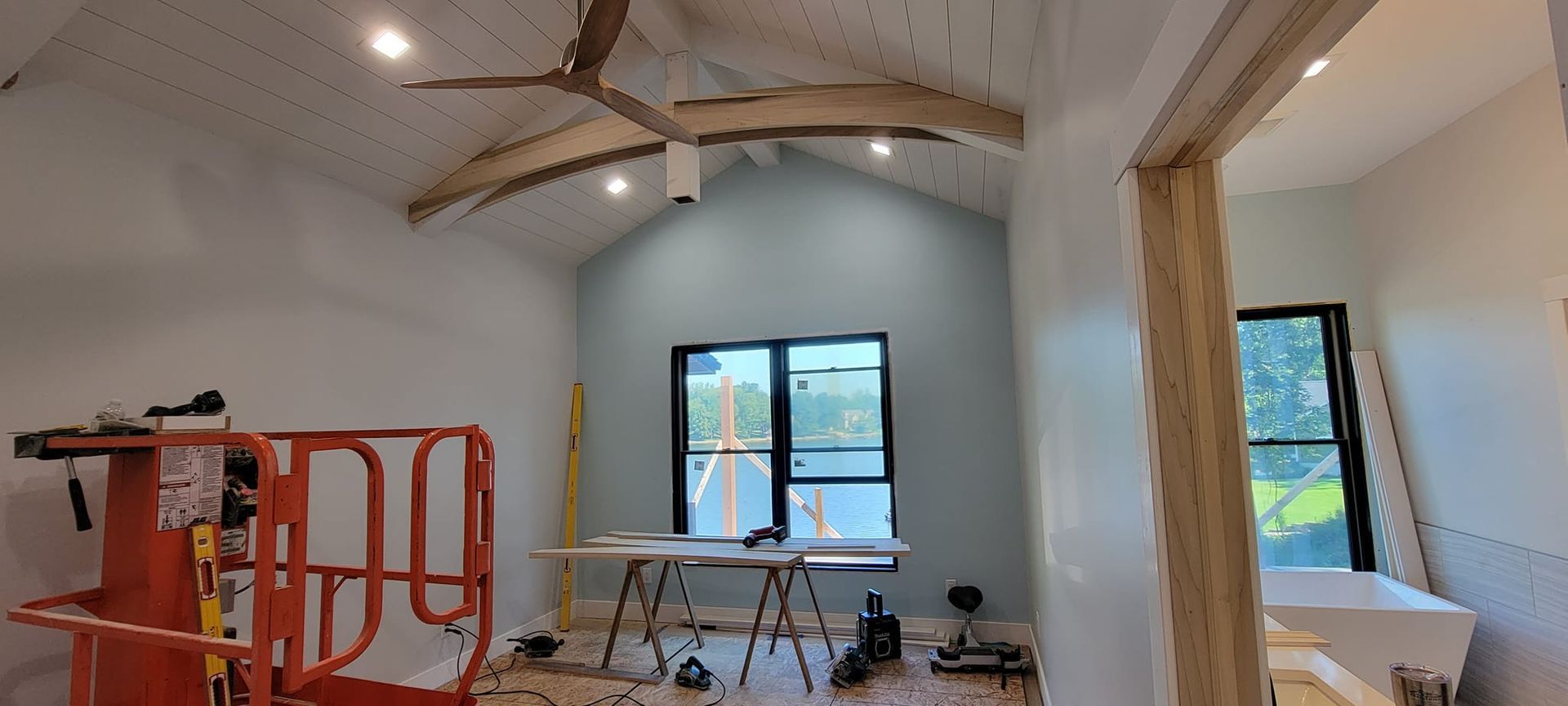 An interior view of a room under construction with white paneled vaulted ceilings, a blue accent wall, and a large window.