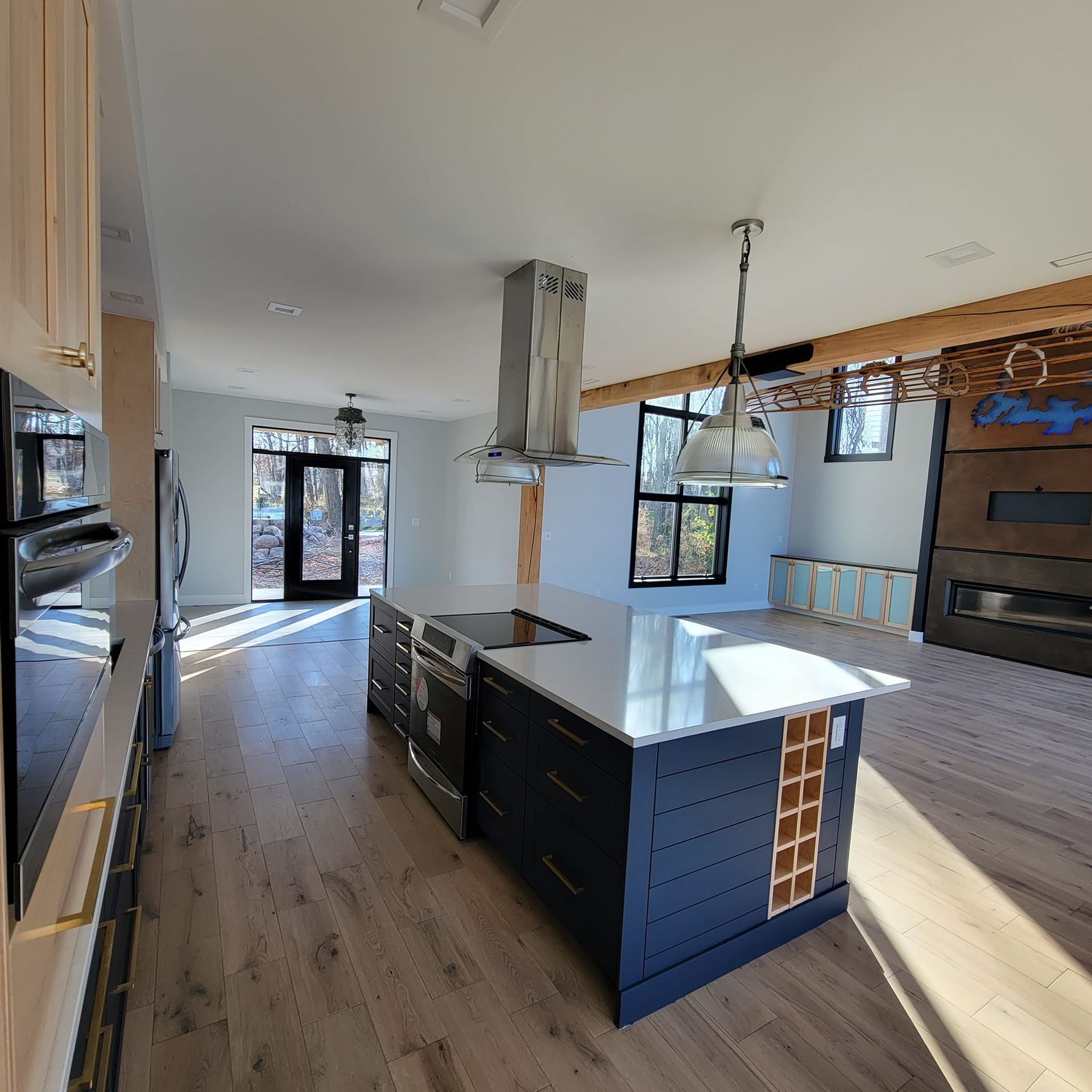 A modern open-concept kitchen with a dark blue island, white countertops, stainless appliances, and light wood floors.