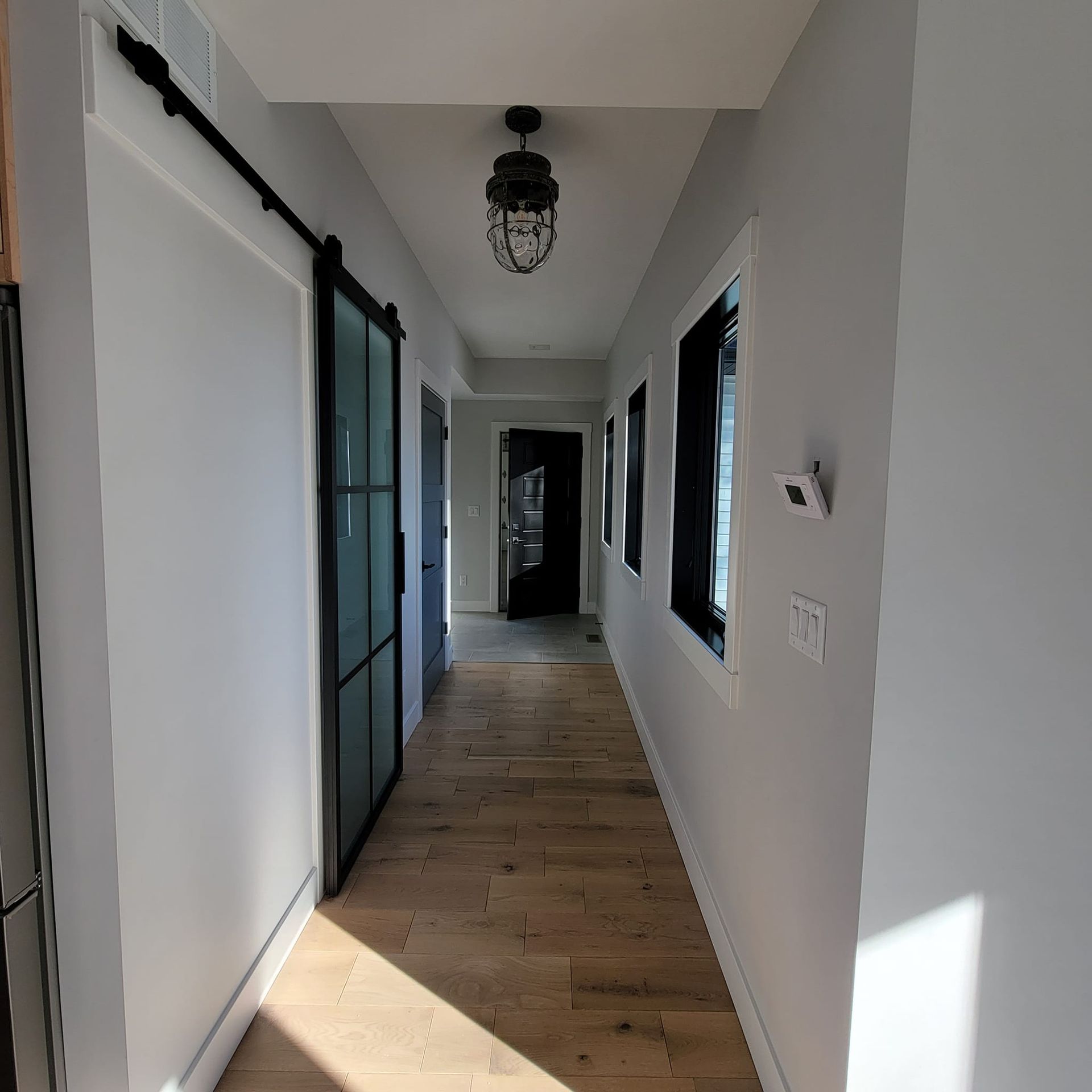 A long hallway with light wood floors, gray walls, a sliding glass barn door, and a black lantern-style pendant light.