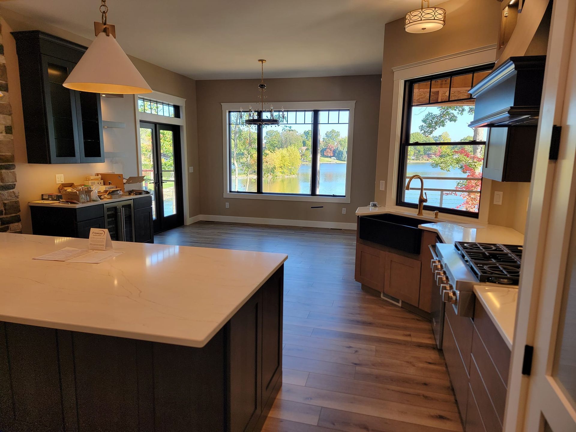 Modern kitchen with a white quartz island, dark cabinets, a corner sink, and a dining area overlooking a lake view.