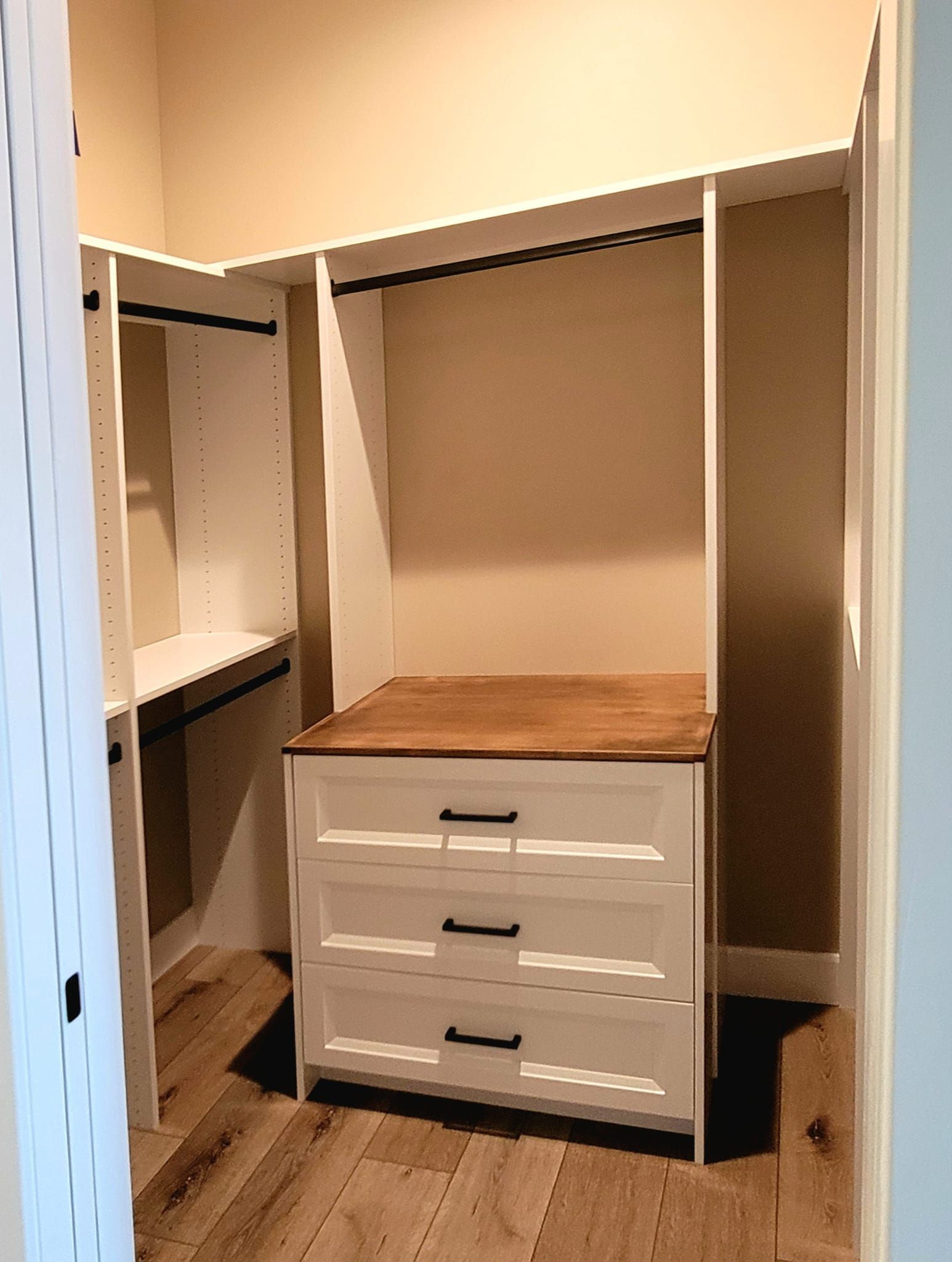 A white walk-in closet featuring a built-in three-drawer dresser with a wooden top and hanging rods on the side walls.