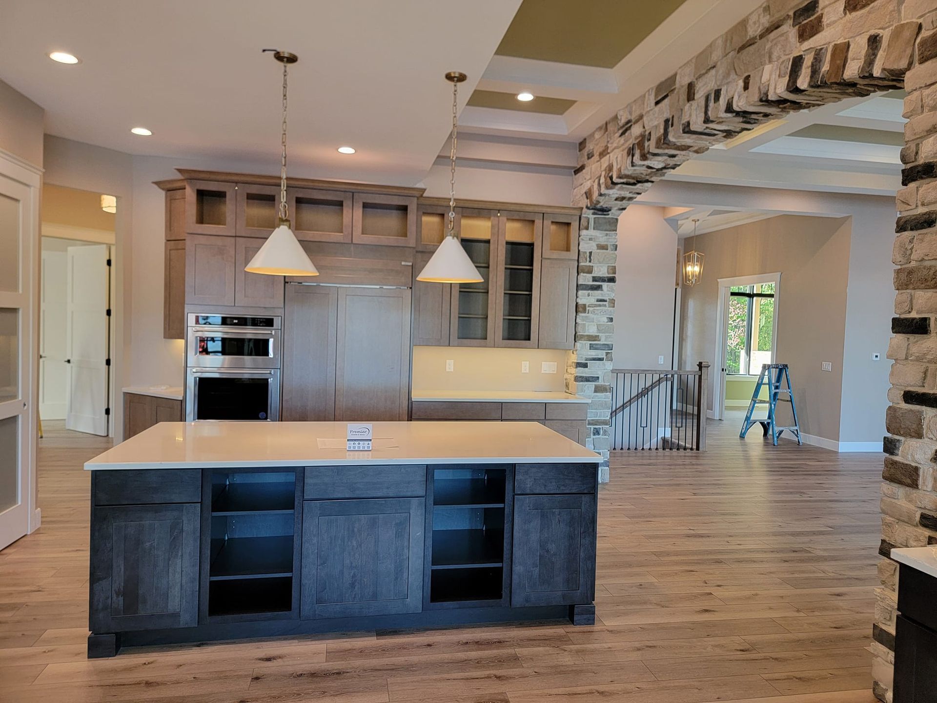 A kitchen featuring a dark blue island with open shelving, light cabinetry, white pendant lights, and a stone archway.