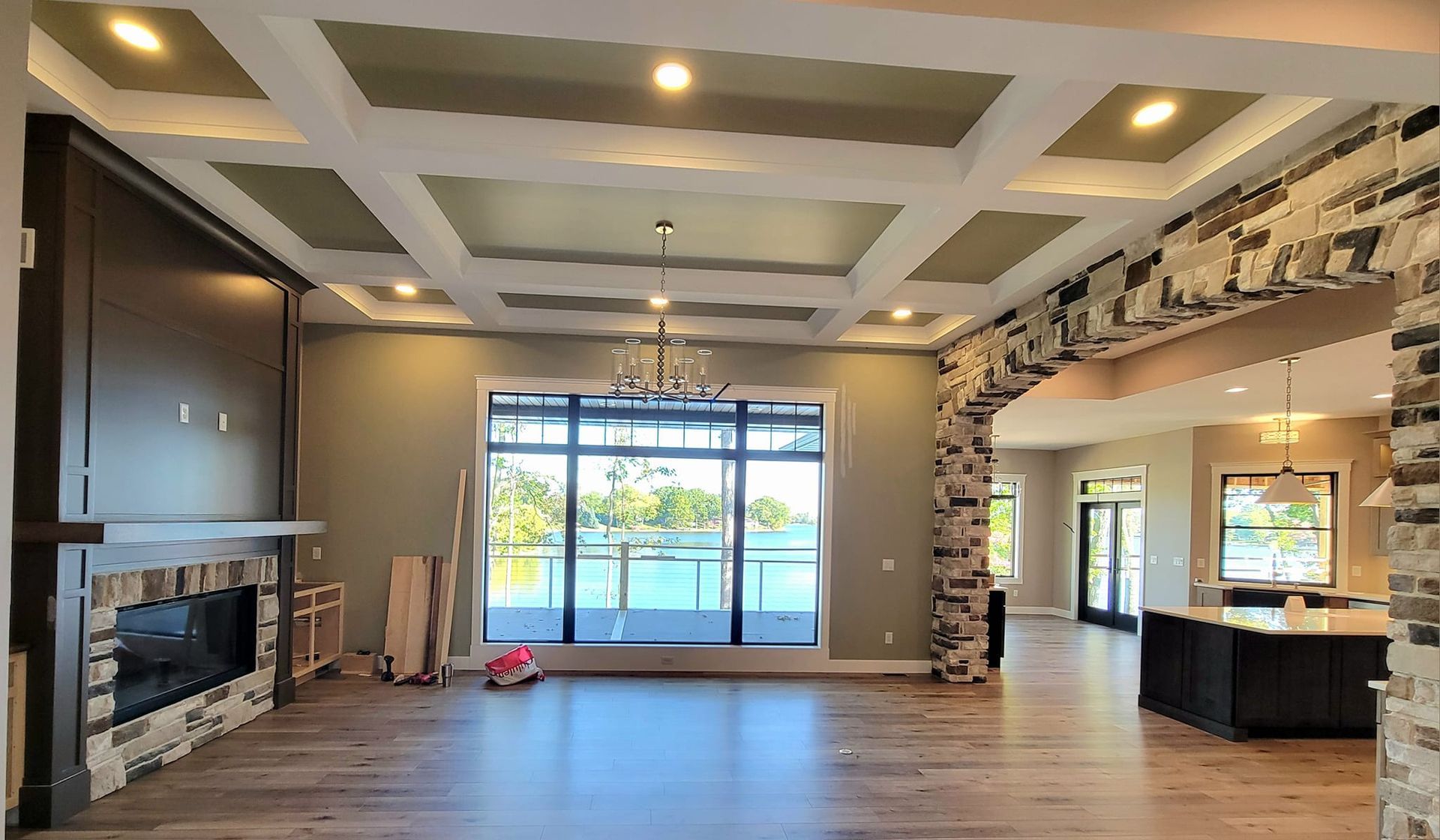 A spacious, open-concept living area with a dark fireplace, stone accents, hardwood floors, and a large view of a lake.