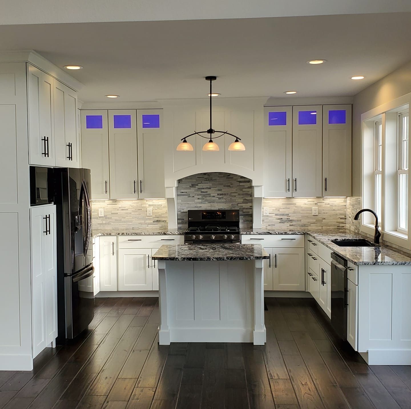 A modern kitchen with white cabinets, dark wood floors, granite countertops, and black appliances.