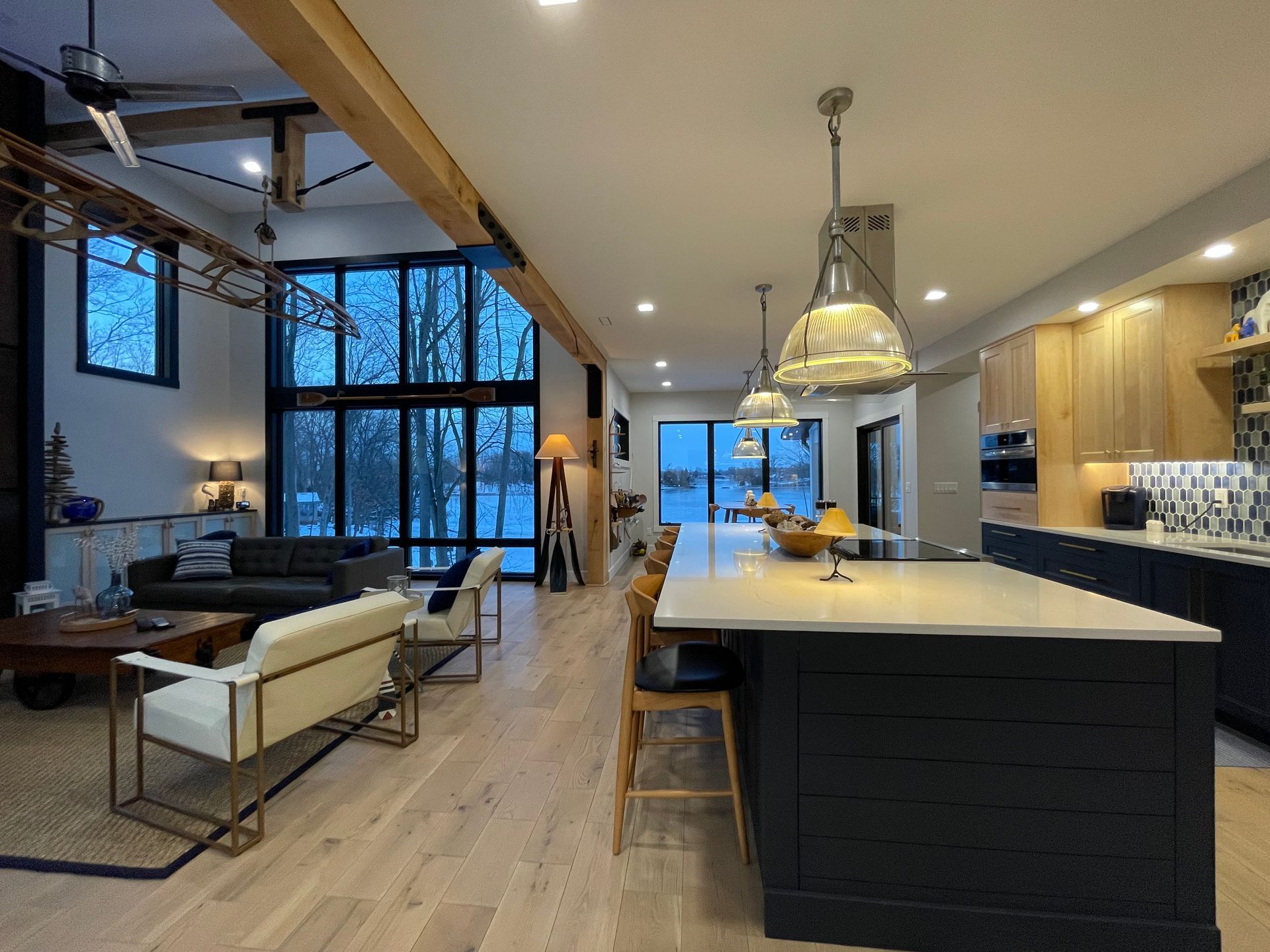 Open-concept living room and kitchen with dark cabinets, a long island, light wood floors, and floor-to-ceiling windows.