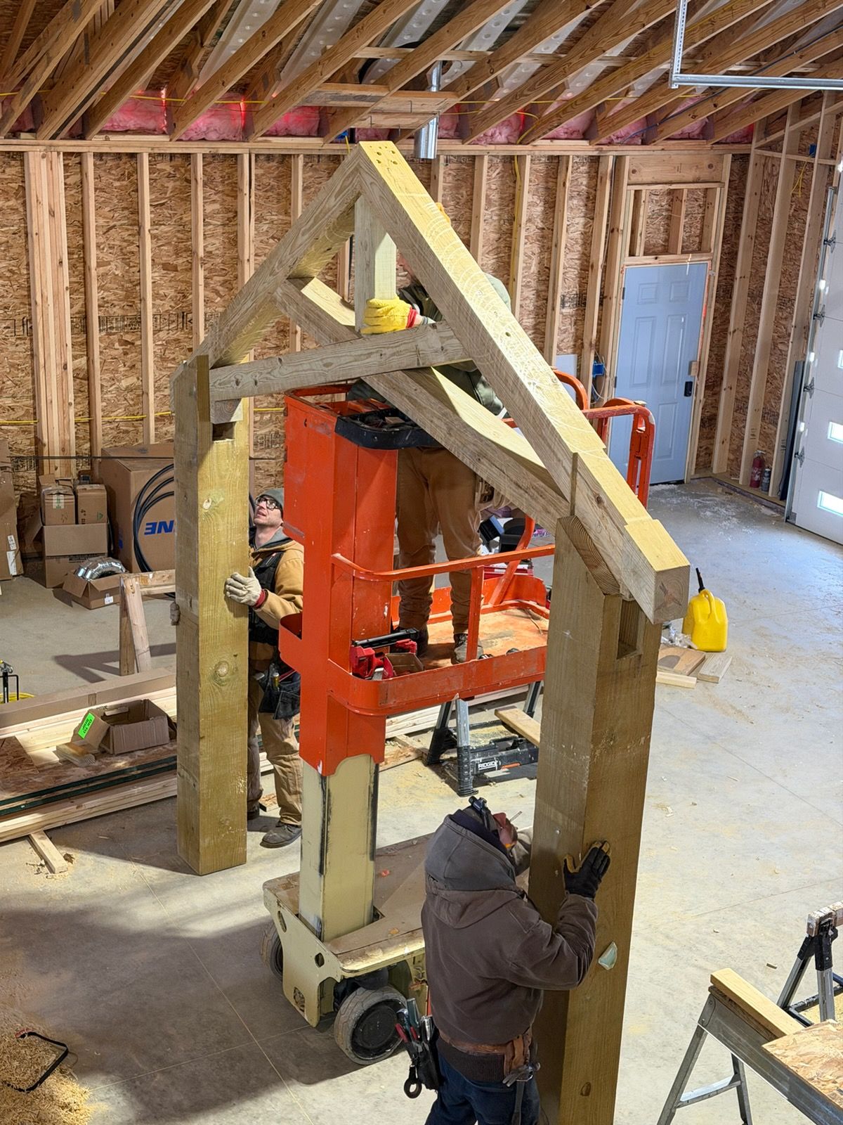 Three construction workers assemble a large wooden post-and-beam frame inside an unfinished building.