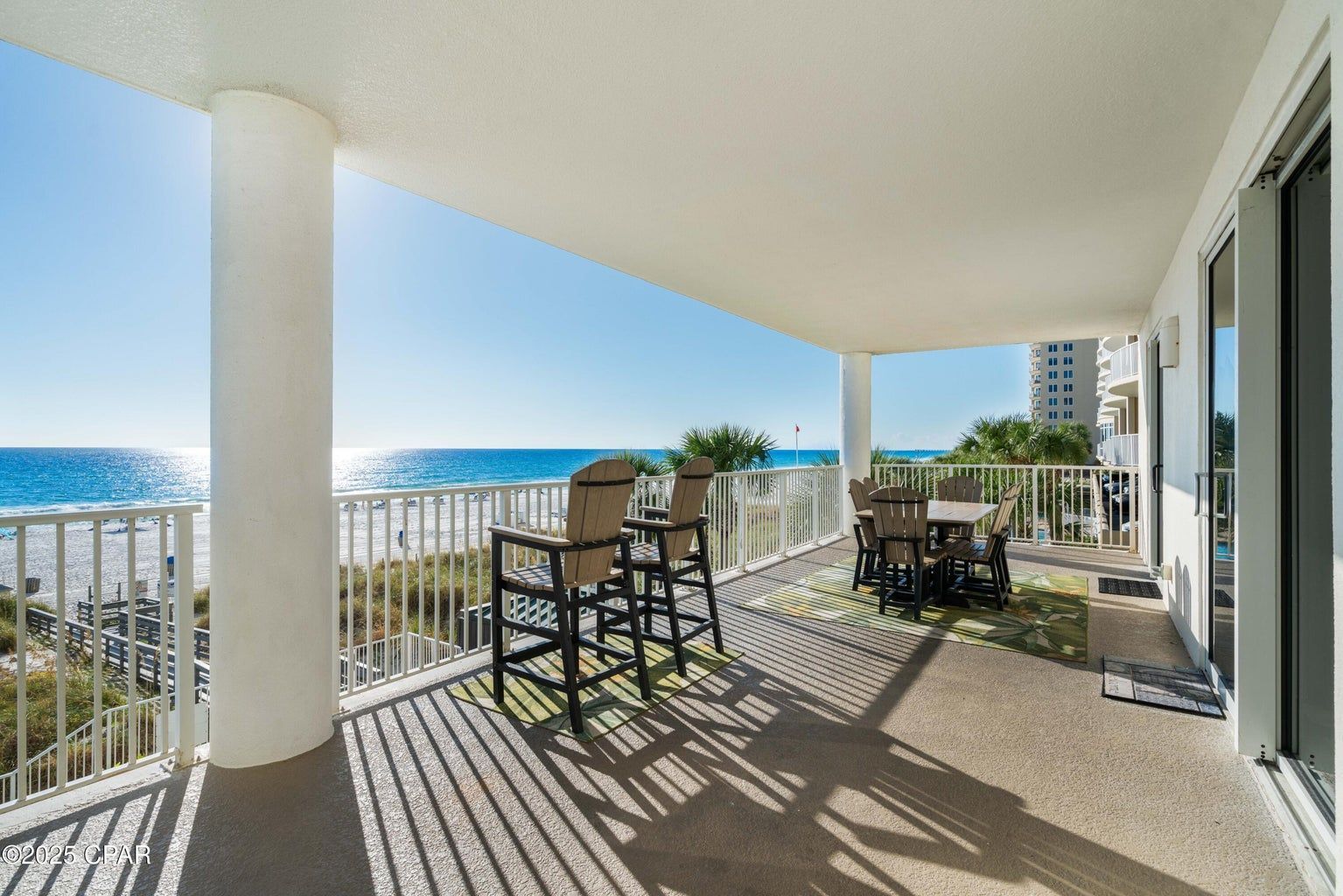 A beautiful condominium balcony view of the Gulf with clear blue skies , gentle rolling water and white beach.
