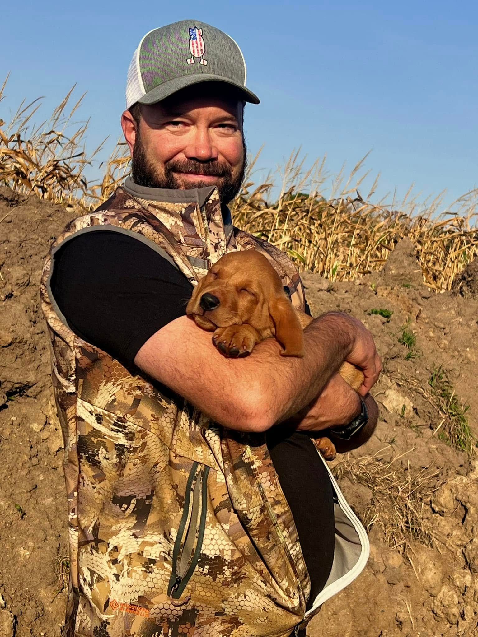 Man in camouflage holding a puppy outdoors.