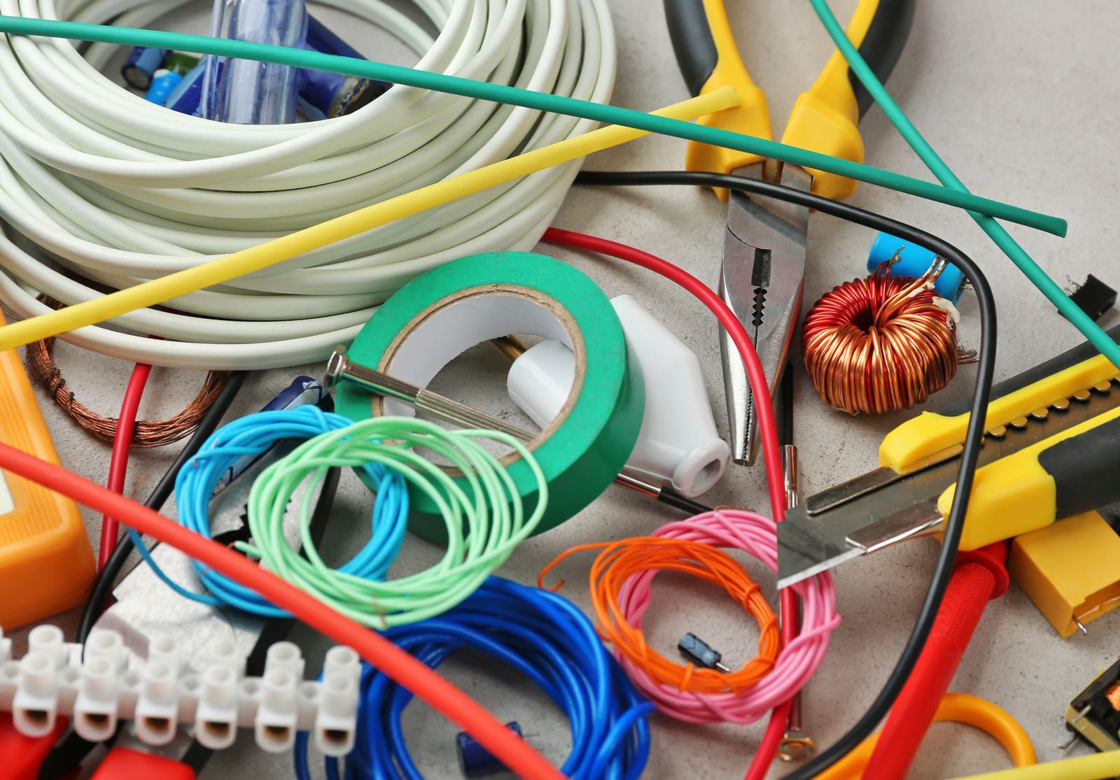 Assorted electrical wires, tools, and tape, including yellow, green, blue, and red, arranged on a surface.