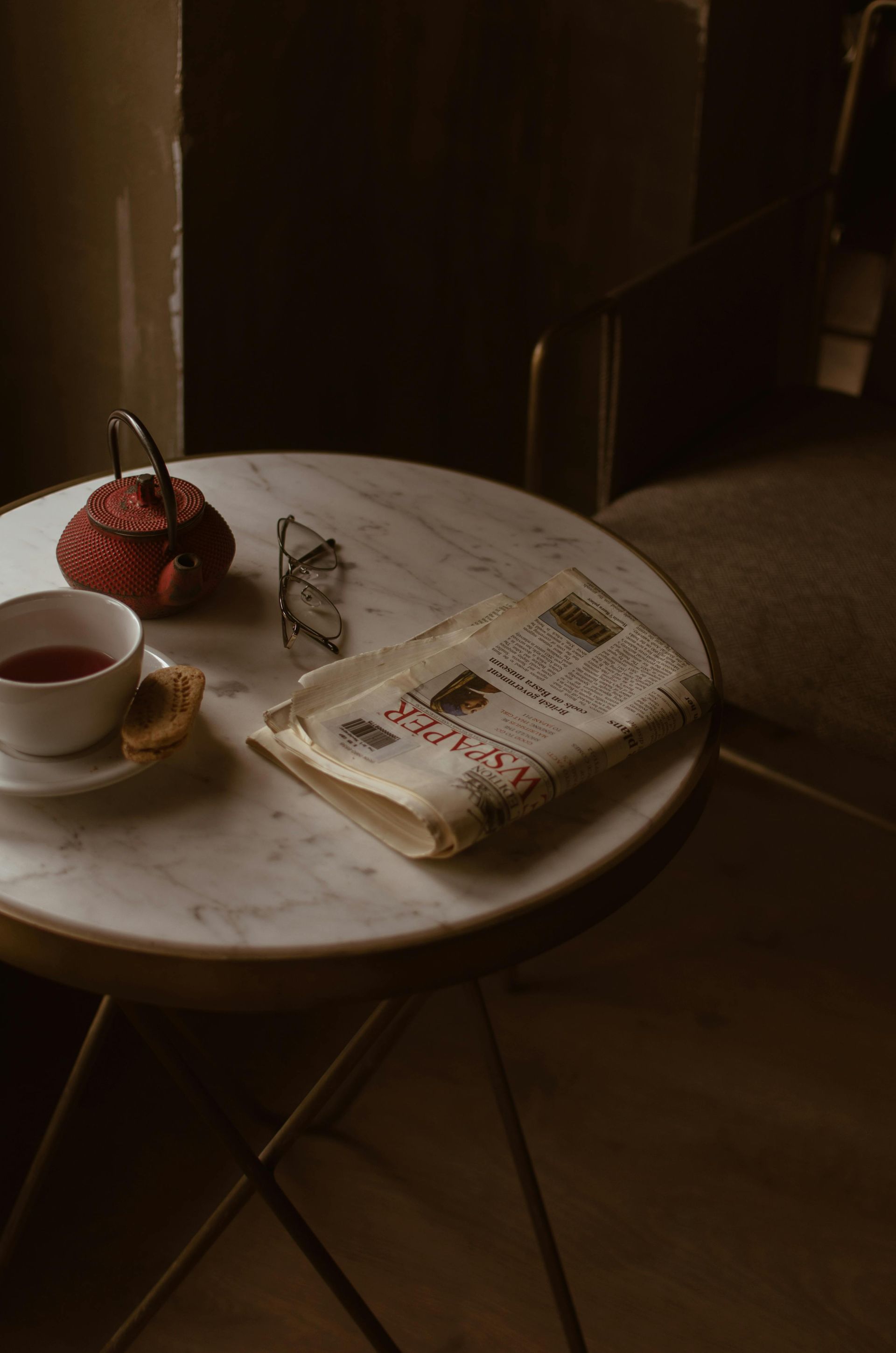 Una mesa con una taza de té, un periódico y vasos encima.