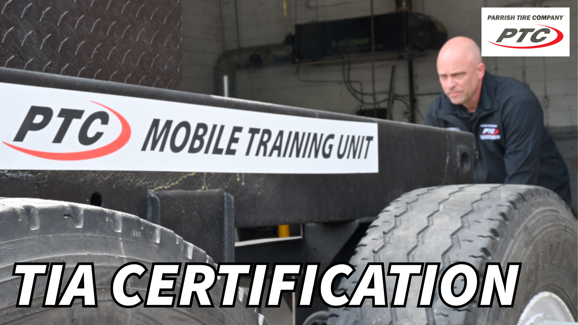 Man in uniform inspects a mobile training unit's tires, TIA certification is the focus, inside a repair shop.