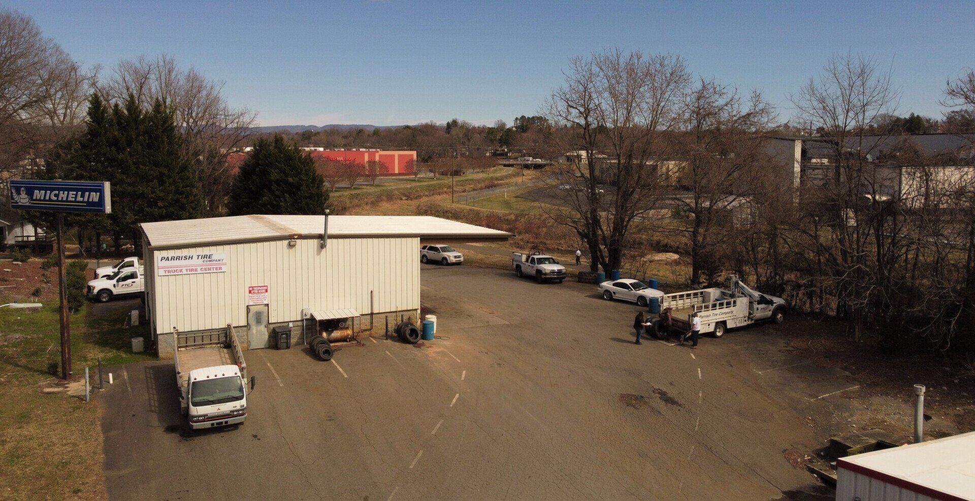 Exterior shot of an auto repair shop on a sunny day. Several service vehicles and people are present.
