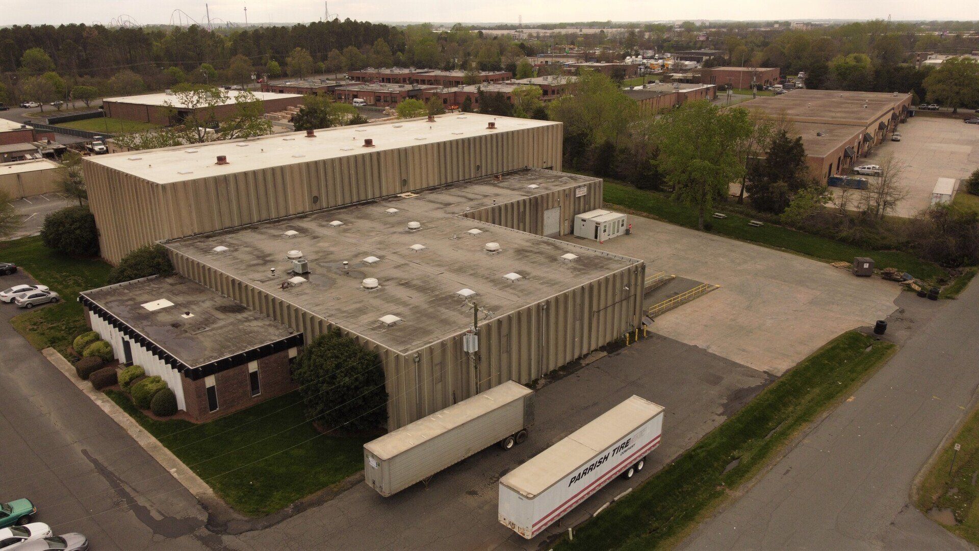 Buildings with industrial-looking siding, two trailers, and parking area, with trees and other buildings in the background.