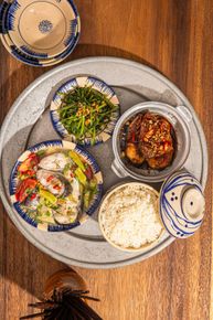 A Vietnamese meal on a large grey tray, featuring steamed fish, stir-fried greens, braised pork, and a bowl of white rice.