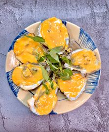 Five oysters topped with melted yellow cheese and garnished with green herbs, served on a blue and white patterned plate.