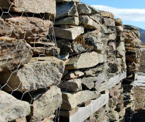 Stone wall with stacked rocks and wire mesh against a blue sky