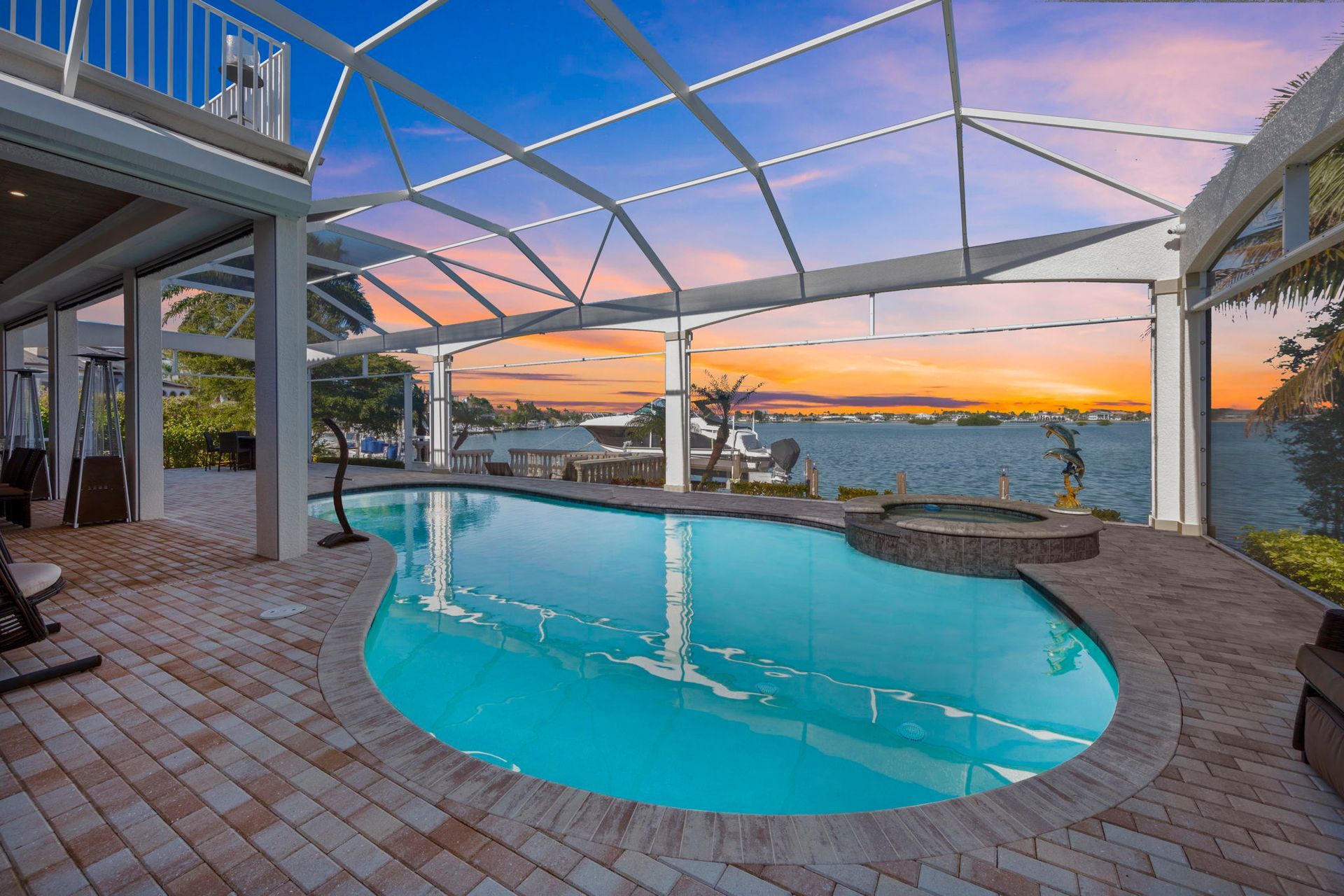 Covered pool patio with a blue spa and sunset view over the water